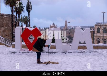 Un jeune touriste prend une photo de selfie à côté d'une sculpture publique contemporaine composée de l'inscription 'I Love JLM' devant les murs de la vieille ville, pendant la chute de neige le 27 janvier 2022, à Jérusalem, en Israël.Jérusalem a été couverte de neige atteignant 10 à 20 centimètres (quatre à huit pouces) pendant la nuit. Banque D'Images