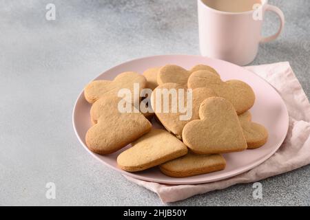 Petit déjeuner de la Saint-Valentin, café avec lait et biscuits en forme de coeur sur plaque rose sur fond gris.Gros plan.Espace pour vos salutations. Banque D'Images