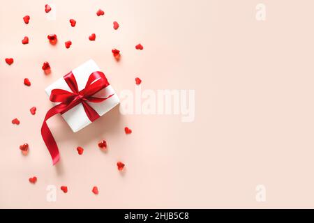 Cadeau de Saint-Valentin avec ruban rouge et confetti en forme de coeur sur fond rose.Bannière.Copier l'espace.Vue de dessus. Banque D'Images