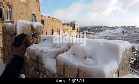 Un homme israélien prend une photo alors qu'il se tient au sommet des murs de la vieille ville pendant la chute de neige du 27 janvier 2022 à Jérusalem, Israël.Jérusalem a été couverte de neige atteignant 10 à 20 centimètres (quatre à huit pouces) pendant la nuit. Banque D'Images