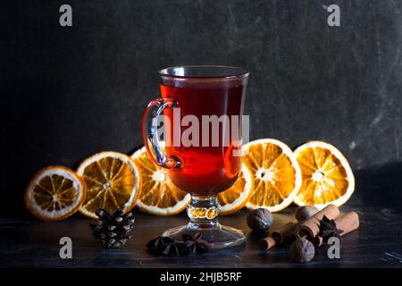 Verre de vin chaud, épices et morceaux d'oranges sur fond noir Banque D'Images