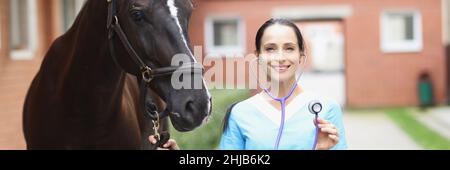 Portrait de jeune femme souriante vétérinaire tenant Steepler tout en se tenant à côté de cheval Banque D'Images