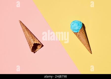Cornets de crème glacée avec une cuillère de crème glacée sur fond rose pastel et jaune.Concept alimentaire d'été minimal.Pose à plat. Banque D'Images