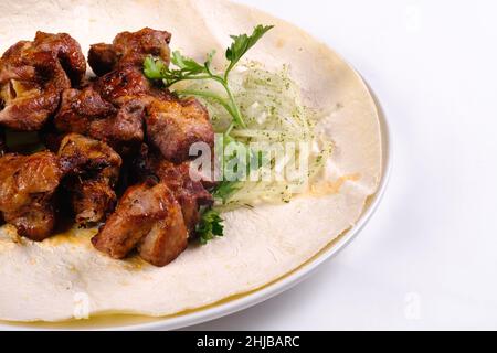 Le kebab de porc sur le lavash se trouve dans une assiette blanche sur un fond blanc isolé. Banque D'Images