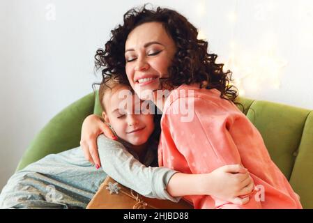 Bonne famille le matin de Noël, jeune mère souriante et petite fille fille qui embrasse les yeux fermés tout en échangeant des cadeaux de Noël à la maison.Maman et Banque D'Images