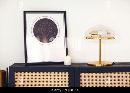 Commode ou commode en bois noir avec affiche carte encadrée d'étoiles, lampe et bougie contre le mur lumineux dans un intérieur contemporain minimaliste.Intérieur des Banque D'Images