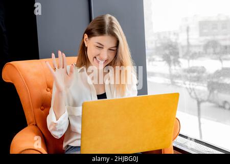 Une femme d'affaires heureuse a une vidéoconférence, utilisant un ordinateur portable et de l'ondulation Bonjour.Une femme ou un étudiant attirante parle avec un collègue ou un ami par le biais de Banque D'Images