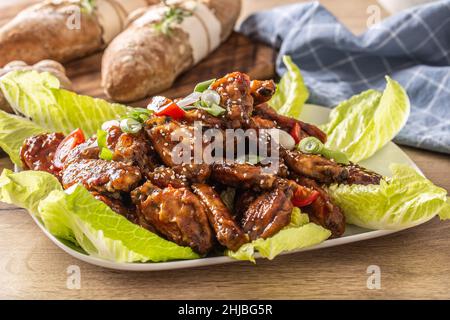 Ailes de poulet asiatiques dans une marinade épicée et collante parsemée de sésame et servie sur des feuilles de salade. Banque D'Images