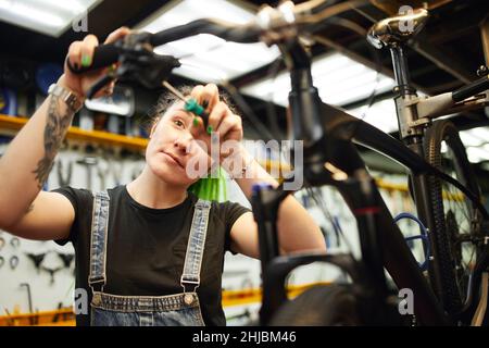 Ravi alternative mécanique féminine avec tatouages et Dreadlocks fixation guidon avec tournevis tout en travaillant dans un atelier de réparation de vélo Banque D'Images