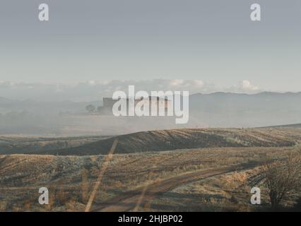 Ferme toscane abandonnée devant les collines vallonnées de Toscane et couverte de brouillard matinal Banque D'Images