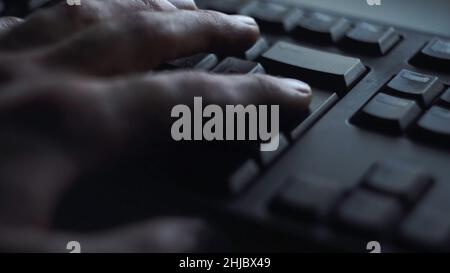 Gros plan, un homme appuie sur la touche du clavier.L'homme appuie sur le bouton pour entrer dans le clavier de l'ordinateur.La main de l'homme appuie sur le clavier à la lumière de l'écran de l'ordinateur. Banque D'Images