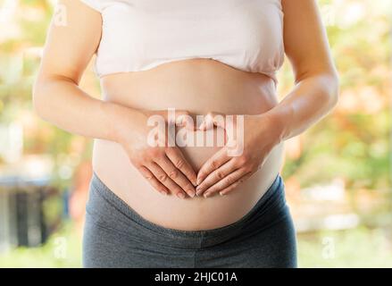 Photo courte d'une femme enceinte touchant son ventre sur un fond naturel clair Banque D'Images