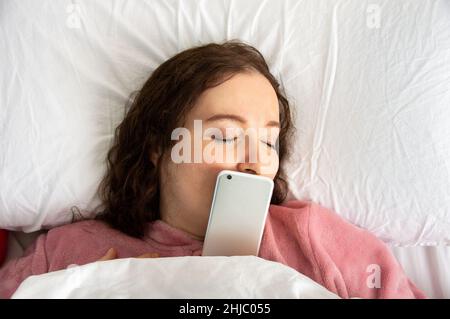 Photo en grand angle d'une jeune femme au lit avec le téléphone sur son visage Banque D'Images