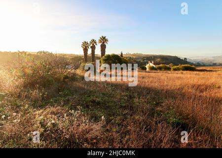 Vue sur le paysage typique de l'Alentejo avec village portugais dans le brouillard du matin un soleil levant au sentier de randonnée de Rota Vicentina près de Carrascalinho, Aljezur Banque D'Images