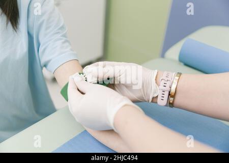 Effectuer un test sanguin sur une veine dans la salle de traitement.L'infirmière pousse une seringue avec une aiguille dans la main du patient.Ecouvillon appuyé contre le Banque D'Images