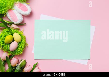 Composition de Pâques.Œufs multicolores dans un nid de fleurs de tulipe oreilles de lapin sur fond rose.Feuille de papier vide avec espace pour le texte et les copies Banque D'Images