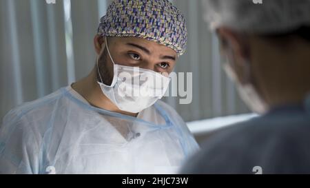 Gros plan de deux chirurgiens masculins regardant vers le bas au travail.Hommes médecins en portant des masques stériles et uniforme pendant la procédure, concept de médecine. Banque D'Images