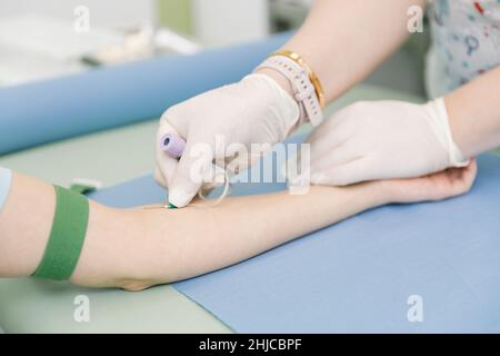 Effectuer un test sanguin sur une veine dans la salle de traitement.L'infirmière pousse une seringue avec une aiguille dans la main du patient.Ecouvillon appuyé contre le Banque D'Images