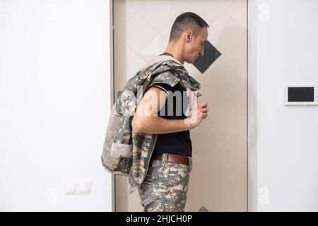 Soldat en camouflage debout près de la porte de la maison Banque D'Images