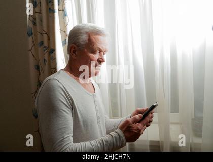 Un homme à la retraite discutant avec ses amis sur les réseaux sociaux, tapant sur son smartphone.Homme senior heureux utilisant le téléphone à la maison. Banque D'Images