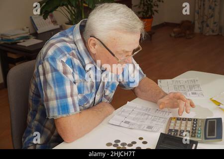 Homme senior assis à la table et calculant les finances.Le vieil homme vérifie les factures.Homme comptant des pièces sur la table.Concept de calcul de la pension Banque D'Images