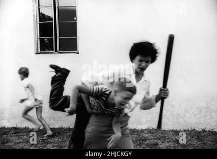 Mère en colère discipline fils après qu'il a cassé la fenêtre des voisins avec un baseball comme un autre enfant s'échappe. Banque D'Images