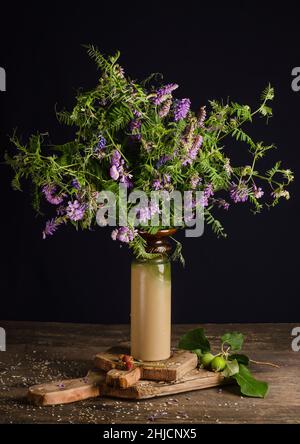 Encore la vie avec un bouquet de fleurs de champ d'été de pois de souris dans un vase sur un fond noir sur une ancienne table en bois vintage. Banque D'Images