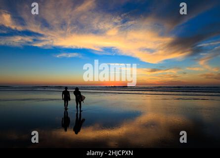 Les surfeurs sur une plage à marée basse et brillante regardent un coucher de soleil d'hiver coloré après avoir surfé à Torrey Pines, San Diego, Californie. Banque D'Images