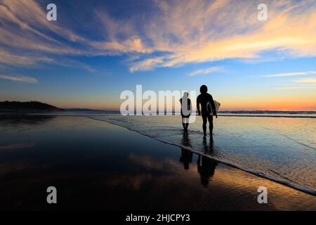 Les surfeurs sur une plage à marée basse et brillante regardent un coucher de soleil d'hiver coloré après avoir surfé à Torrey Pines, San Diego, Californie. Banque D'Images