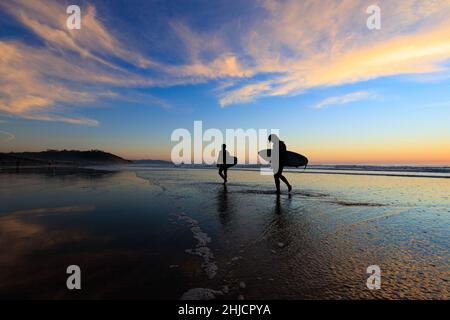 Les surfeurs sur une plage à marée basse et brillante regardent un coucher de soleil d'hiver coloré après avoir surfé à Torrey Pines, San Diego, Californie. Banque D'Images