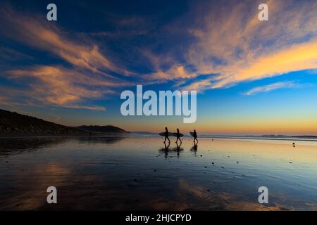 Les surfeurs sur une plage à marée basse et brillante regardent un coucher de soleil d'hiver coloré après avoir surfé à Torrey Pines, San Diego, Californie. Banque D'Images