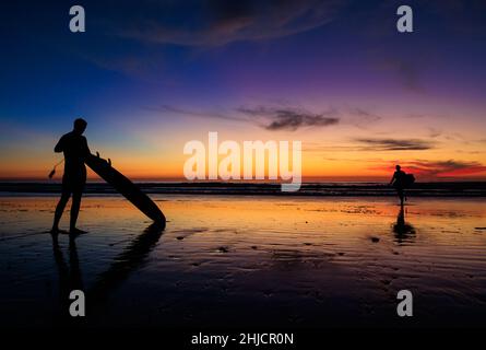 Les surfeurs sur une plage à marée basse et brillante regardent un coucher de soleil d'hiver coloré après avoir surfé à Torrey Pines, San Diego, Californie. Banque D'Images