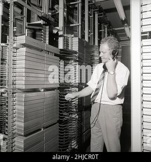 Téléphonie dans le 1970s.Homme dans une pièce avec un tableau de commutation automatique reliant les appels via un dispositif mécanique qui connecte les pièces d'appel et de réception.Le fabricant est LM Ericsson.Suède 1971 Kristoffersson ref. Ed Banque D'Images