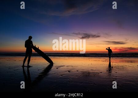 Les surfeurs sur une plage à marée basse et brillante regardent un coucher de soleil d'hiver coloré après avoir surfé à Torrey Pines, San Diego, Californie. Banque D'Images