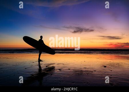 Les surfeurs sur une plage à marée basse et brillante regardent un coucher de soleil d'hiver coloré après avoir surfé à Torrey Pines, San Diego, Californie. Banque D'Images