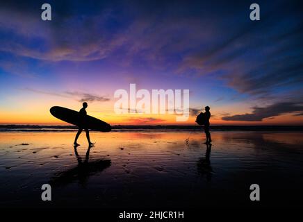 Les surfeurs sur une plage à marée basse et brillante regardent un coucher de soleil d'hiver coloré après avoir surfé à Torrey Pines, San Diego, Californie. Banque D'Images