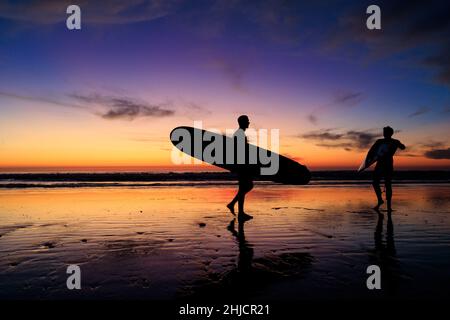 Les surfeurs sur une plage à marée basse et brillante regardent un coucher de soleil d'hiver coloré après avoir surfé à Torrey Pines, San Diego, Californie. Banque D'Images