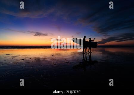 Les surfeurs sur une plage à marée basse et brillante regardent un coucher de soleil d'hiver coloré après avoir surfé à Torrey Pines, San Diego, Californie. Banque D'Images