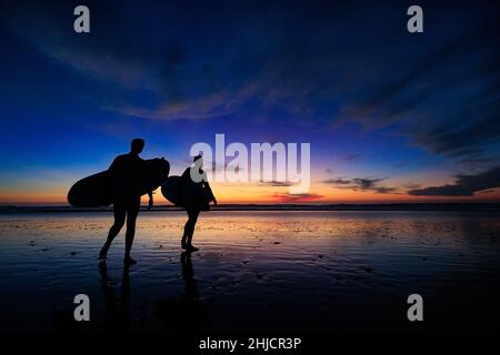 Les surfeurs sur une plage à marée basse et brillante regardent un coucher de soleil d'hiver coloré après avoir surfé à Torrey Pines, San Diego, Californie. Banque D'Images