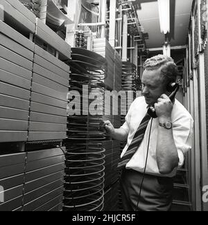 Téléphonie dans le 1970s.Homme dans une pièce avec un tableau de commutation automatique reliant les appels via un dispositif mécanique qui connecte les pièces d'appel et de réception.Le fabricant est LM Ericsson.Suède 1971 Kristoffersson ref. Ed Banque D'Images