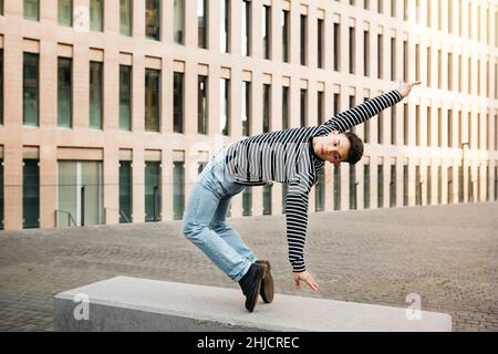 Jeune homme faisant de la danse acrobatique sur un banc de rue Banque D'Images