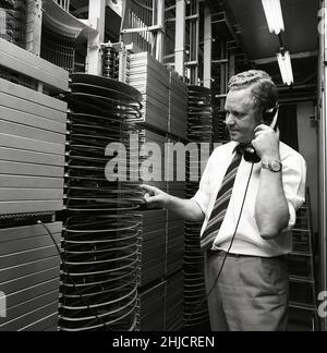 Téléphonie dans le 1970s.Homme dans une pièce avec un tableau de commutation automatique reliant les appels via un dispositif mécanique qui connecte les pièces d'appel et de réception.Le fabricant est LM Ericsson.Suède 1971 Kristoffersson ref. Ed Banque D'Images