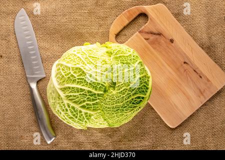 Une tête de chou de Savoie mûre avec un couteau et une planche à découper en bois sur un burlap, macro, vue de dessus. Banque D'Images