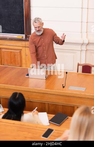Professeur utilisant un ordinateur portable près des étudiants flous dans l'université Banque D'Images