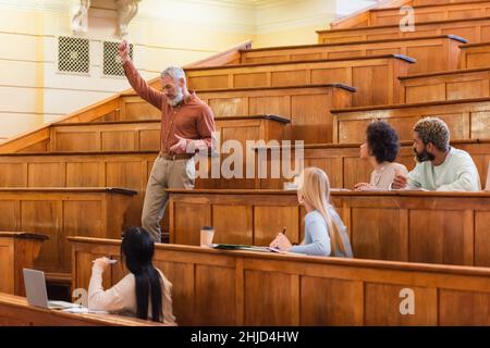 Professeur mature parlant pendant la conférence près d'étudiants multiethniques à l'université Banque D'Images