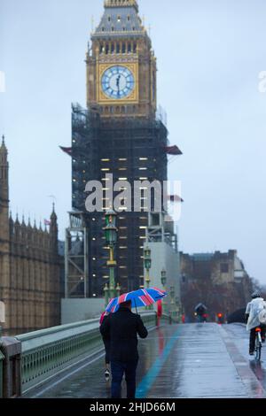 La tour Elizabeth, communément appelée Big Ben, est considérée comme un piéton tenant un drapeau de l'Union marche le long du pont de Westminster dans le centre de Londres. Banque D'Images