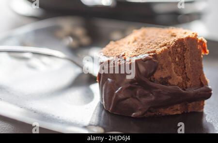 Une tranche d'un gâteau au chocolat avec glaçage au caramel sur une assiette noire.Fourche floue en arrière-plan. Banque D'Images