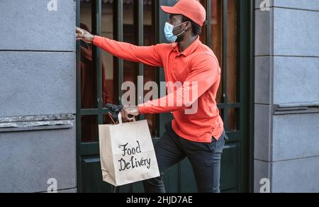 Un cavalier africain qui fournit un repas aux clients avec un scooter électrique tout en portant un masque facial pendant l'épidémie de virus corona Banque D'Images