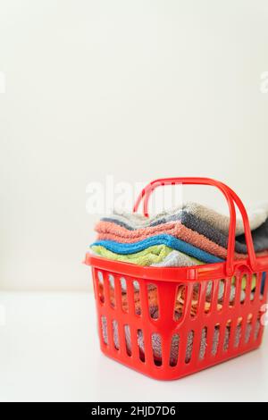 Les serviettes multicolores sont dans un panier à linge rouge sur fond blanc.Blanchisserie et repassage Banque D'Images