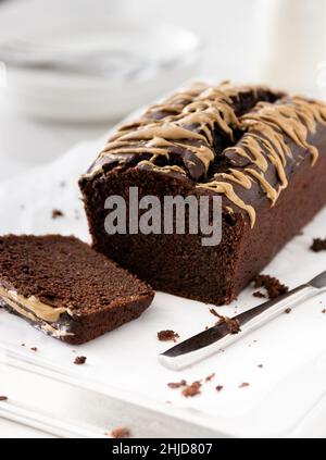 pain de courgettes au chocolat maison avec glaçure, lait et assiettes/fourchettes en arrière-plan Banque D'Images
